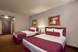 Habitación de hotel con dos camas, una puerta, una lámpara y dos cuadros en la pared.