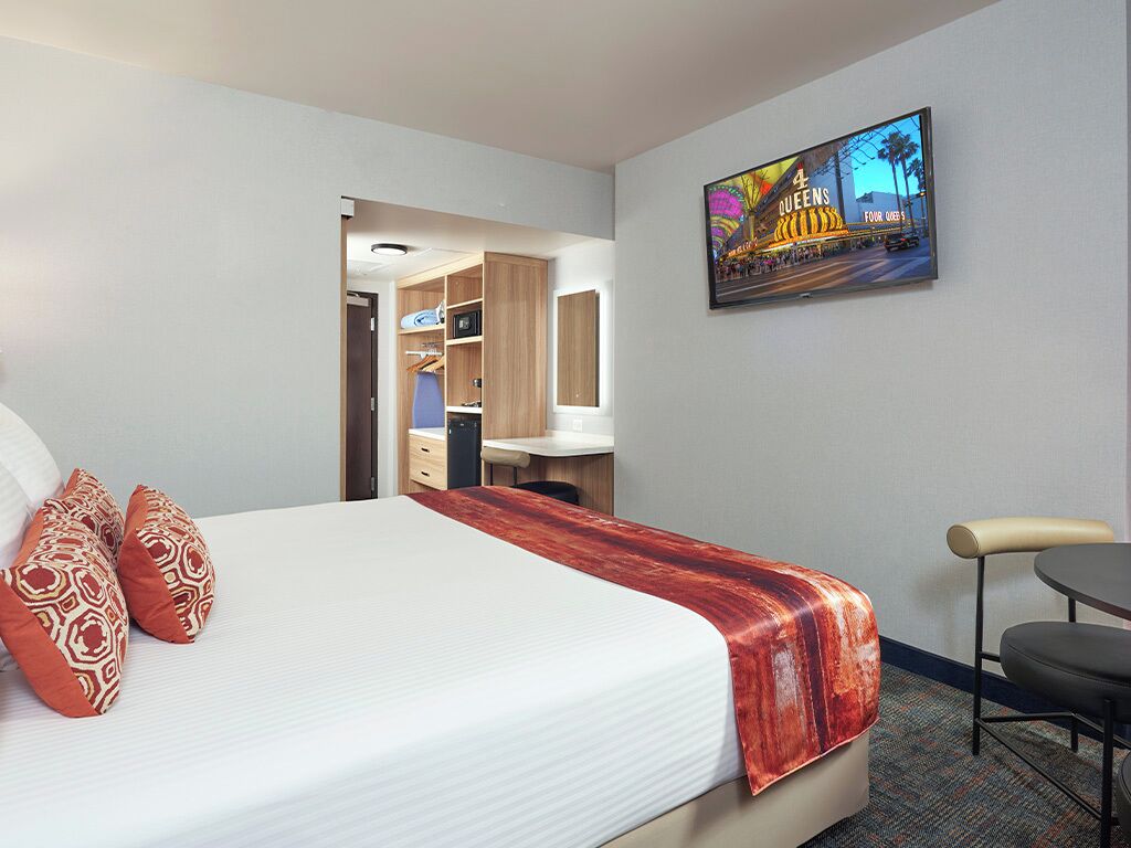 A hotel room with a bed, a desk, and a chair. There is a painting on the wall and a door leading to a bathroom.