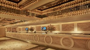 A spacious lobby with a grand reception desk, multiple floors, and a modern chandelier design.