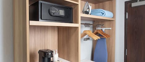 Une chambre d’hôtel avec une armoire en bois, une machine à café, un jeu de clés et une serviette pliée posée sur l’étagère.