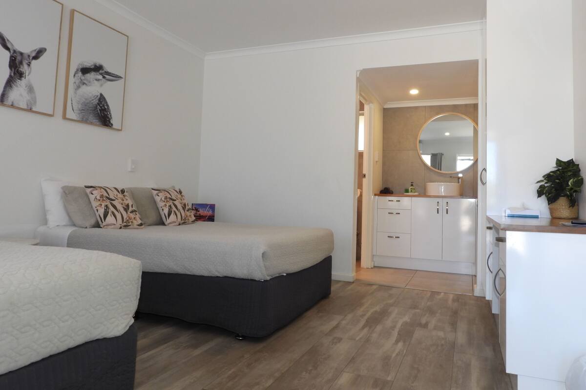 A bedroom with two beds, a sofa, a small table, and a bathroom visible through an open door.