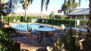 A pool area with a circular table and chairs, surrounded by a fence and palm trees. - Alice Motor Inn (East Side)