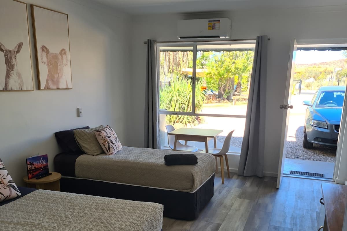 A room with two beds, a table, chairs, and a view of the outside.