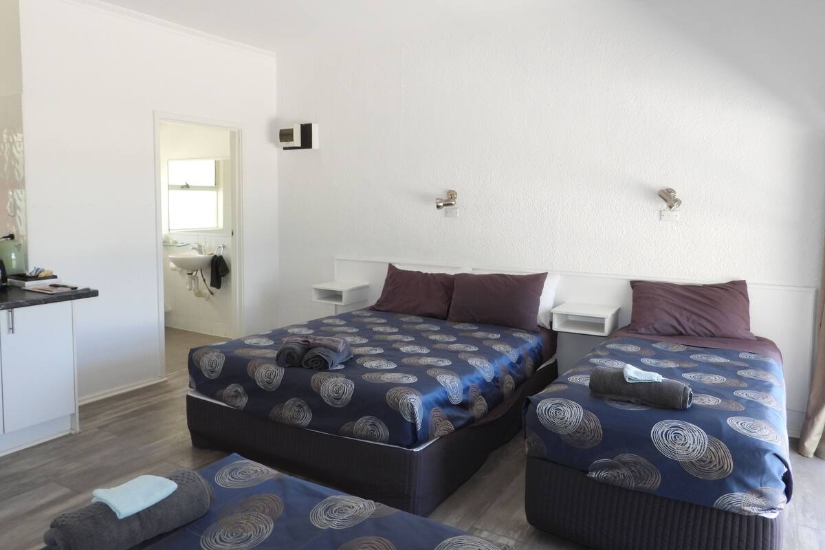 A hotel room with two beds, a small desk, and a bathroom visible through an open door.
