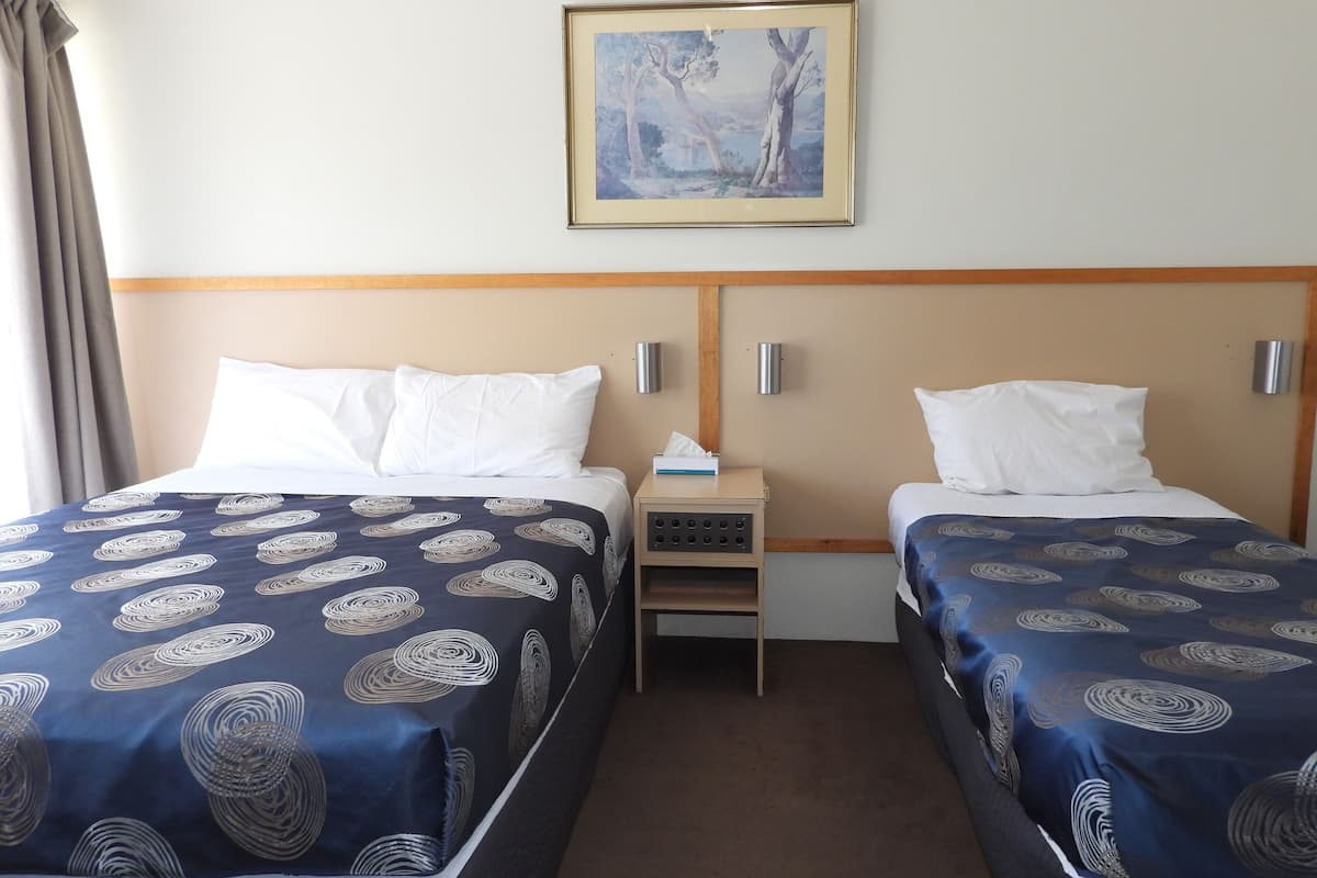 A hotel room with two beds, a nightstand, a painting, and a window with curtains.