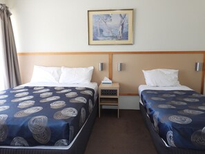 Une chambre d’hôtel avec deux lits, chacun recouvert d’une couvre-lit à motifs, une table de chevet avec une lampe et un tableau accroché au mur.