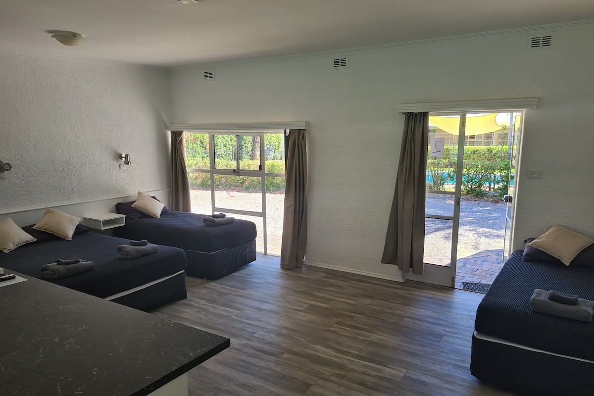 A hotel room with two beds, a small table, and a view of the outdoor area.