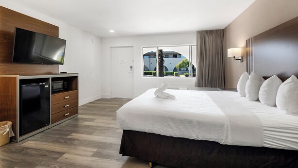 A hotel room with a bed, a TV, a minibar, and a window with a view of the outside. - Heritage Inn Express Roseville (Roseville)