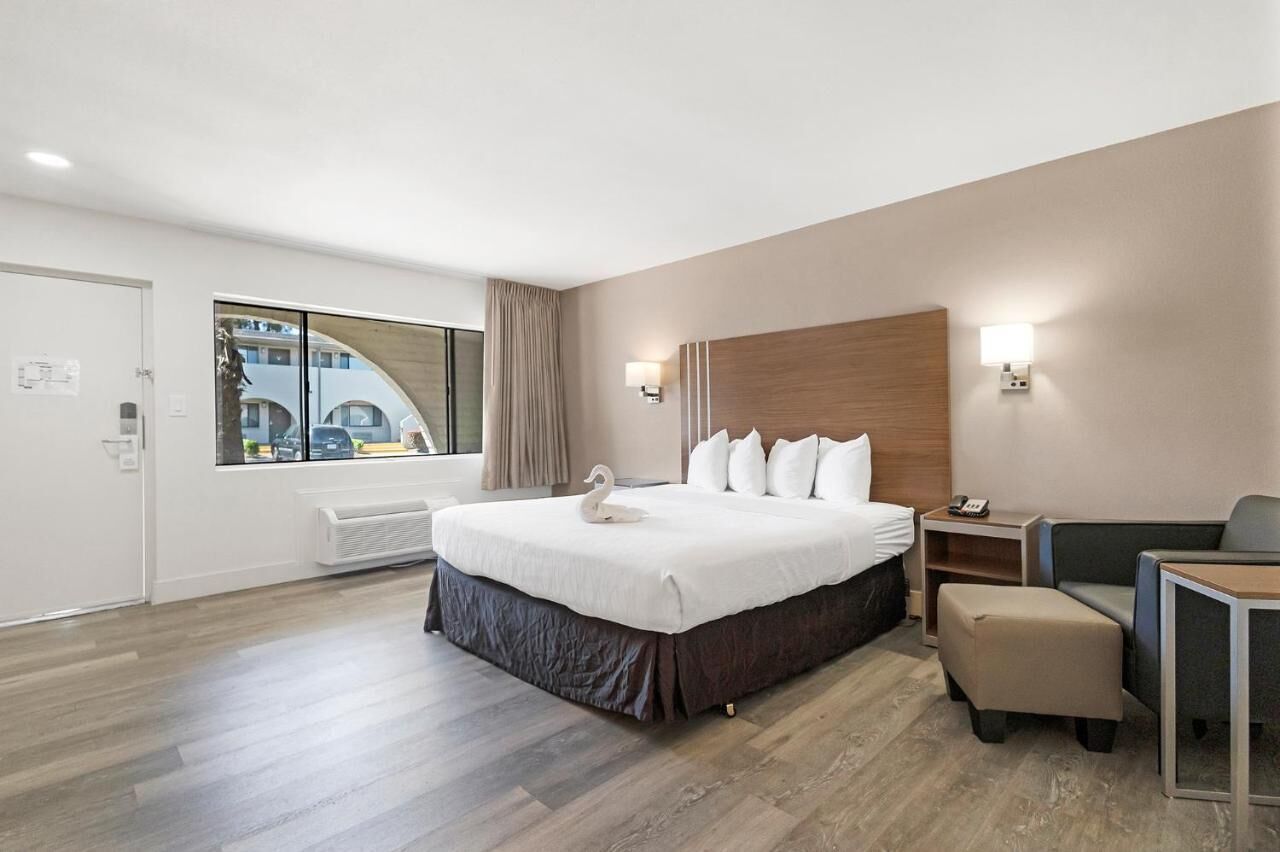 Habitación de hotel con una cama grande, un escritorio, una silla, una ventana con vistas y una lámpara de pared.
