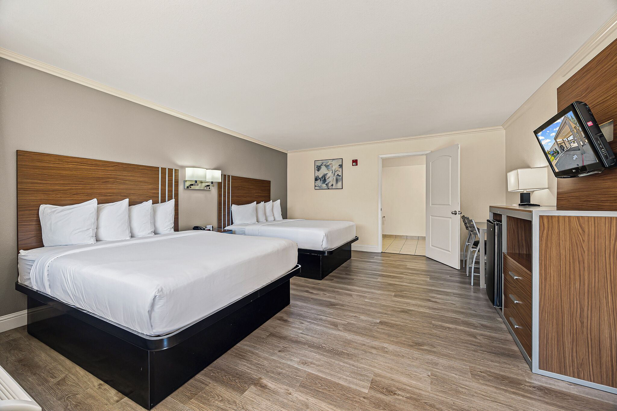 Een hotelkamer met twee bedden, een bureau, een televisie en een deur naar een badkamer.