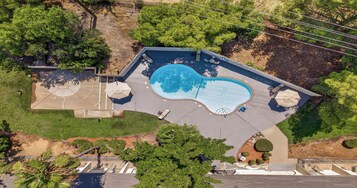 An aerial view of a residential property with a swimming pool, patio furniture, and surrounding greenery.
