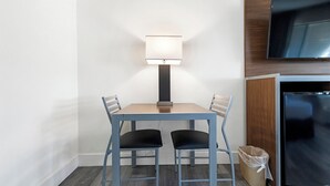 A hotel room with a wooden cabinet, a flat-screen TV, a table with two chairs, and a floor lamp. - Heritage Inn Express Roseville (Roseville)