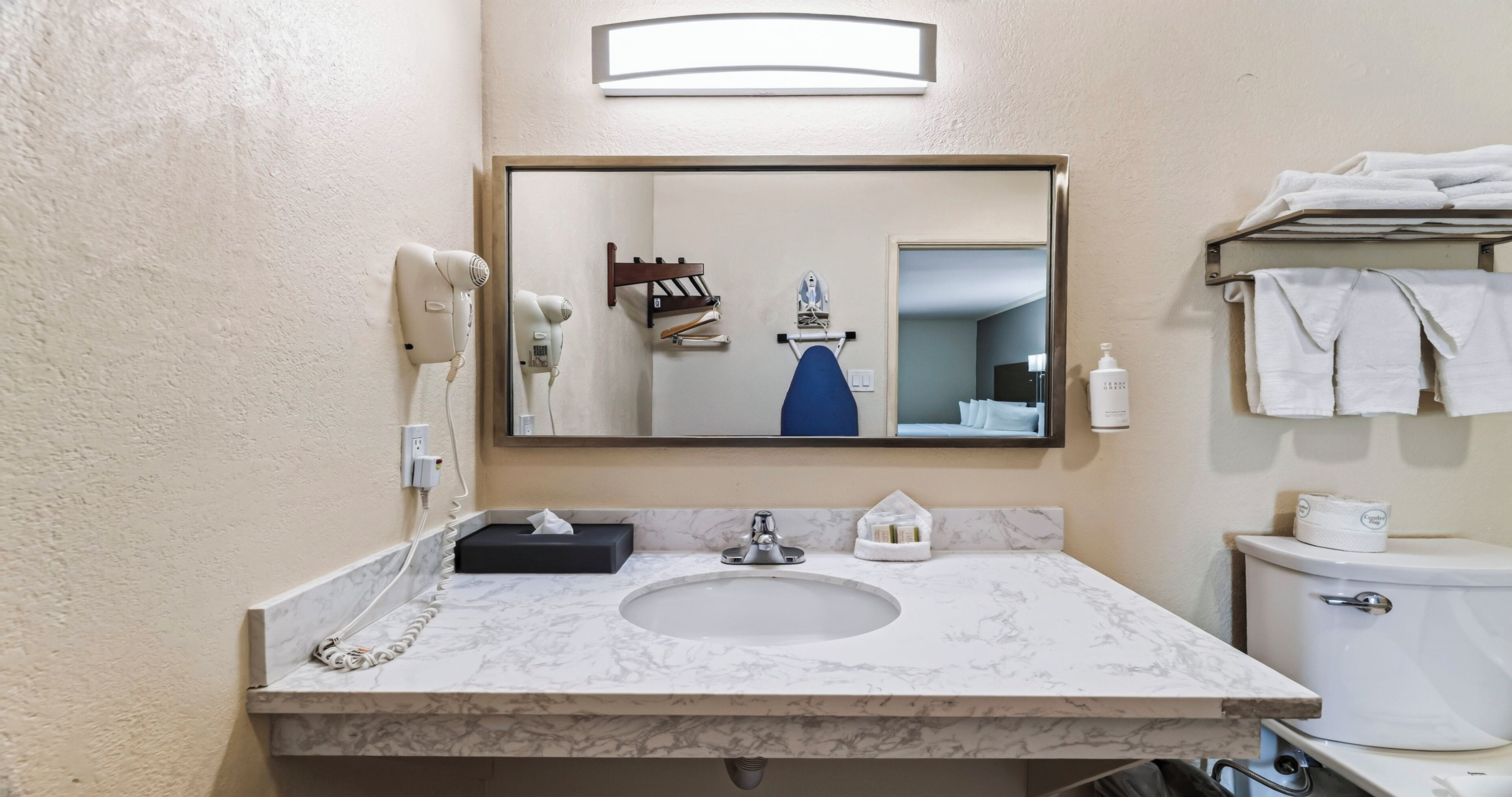 Un baño con lavamanos de mármol, un espejo, secador de pelo, toallero y un inodoro.