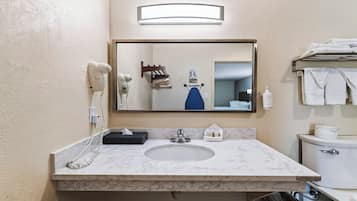 Un baño con lavamanos de mármol, un espejo, secador de pelo, toallero y un inodoro.