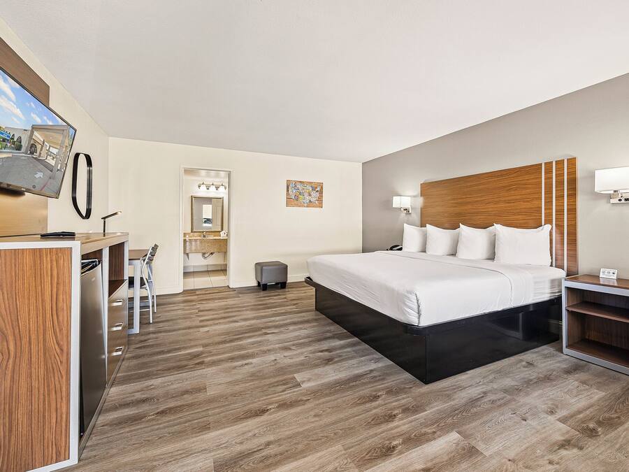 A hotel room with a bed, bedside table, desk, chair, and a television mounted on the wall.