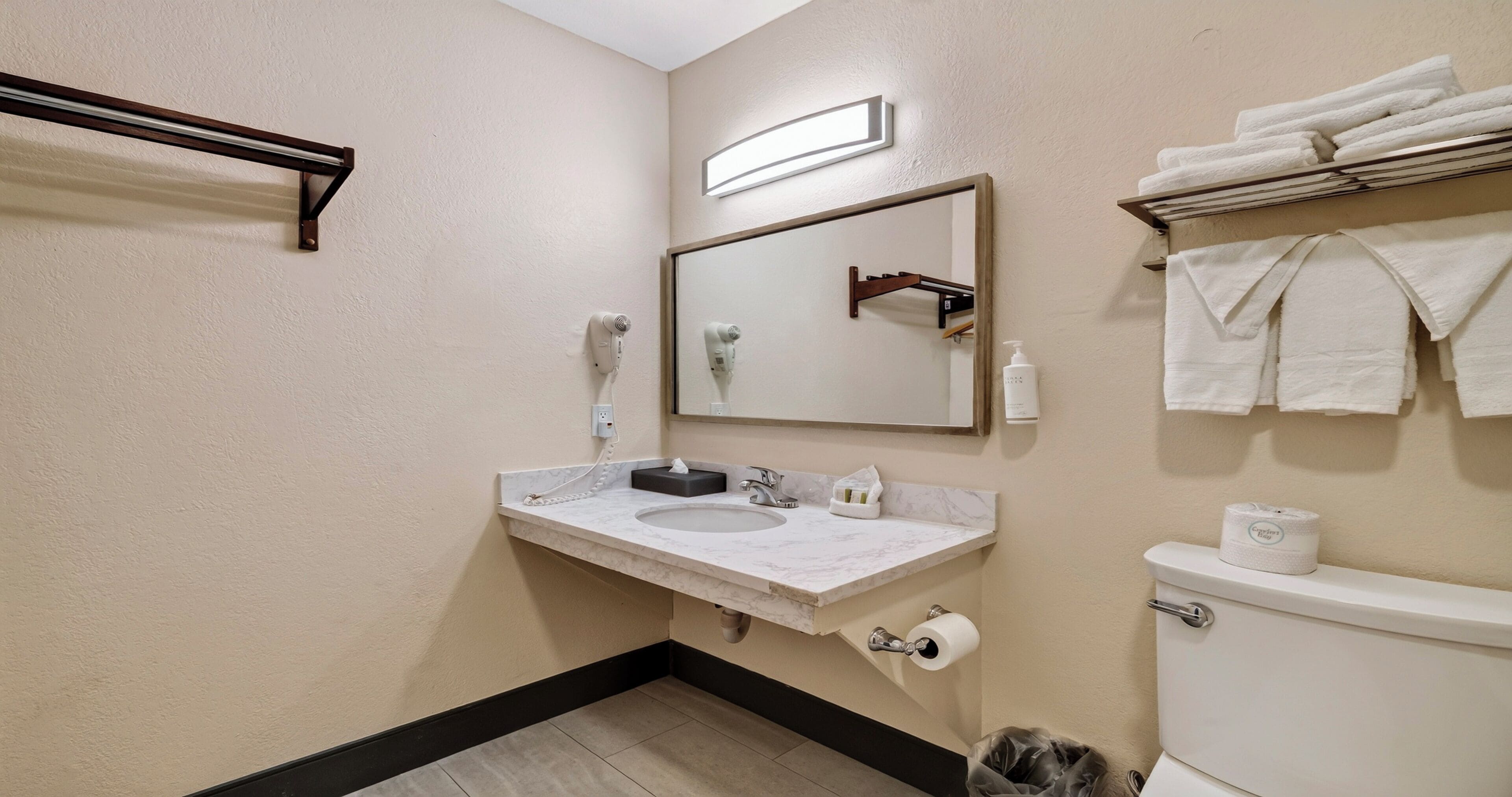 Un bagno con lavandino, specchio, asciugamano, water e cestino.