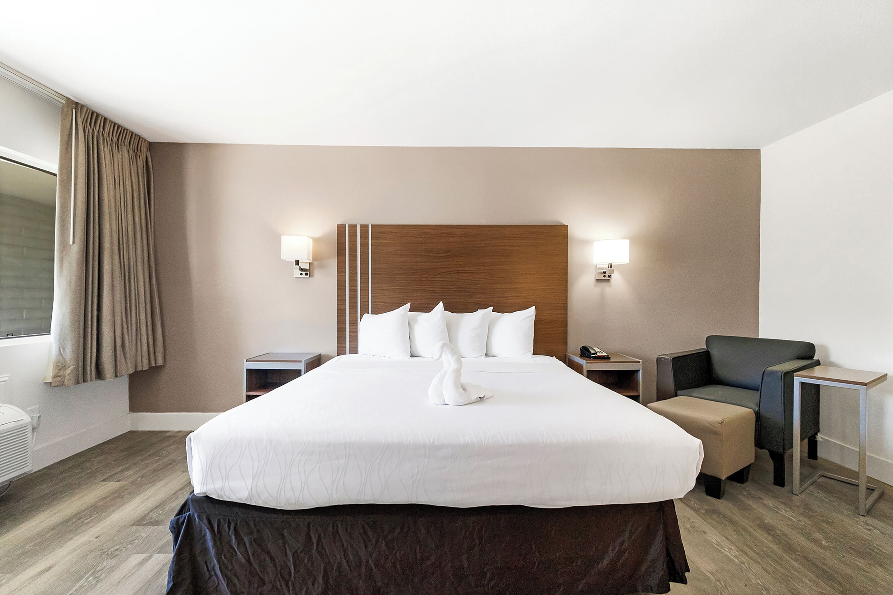 A hotel room with a large bed, two bedside tables, a chair, and a desk.