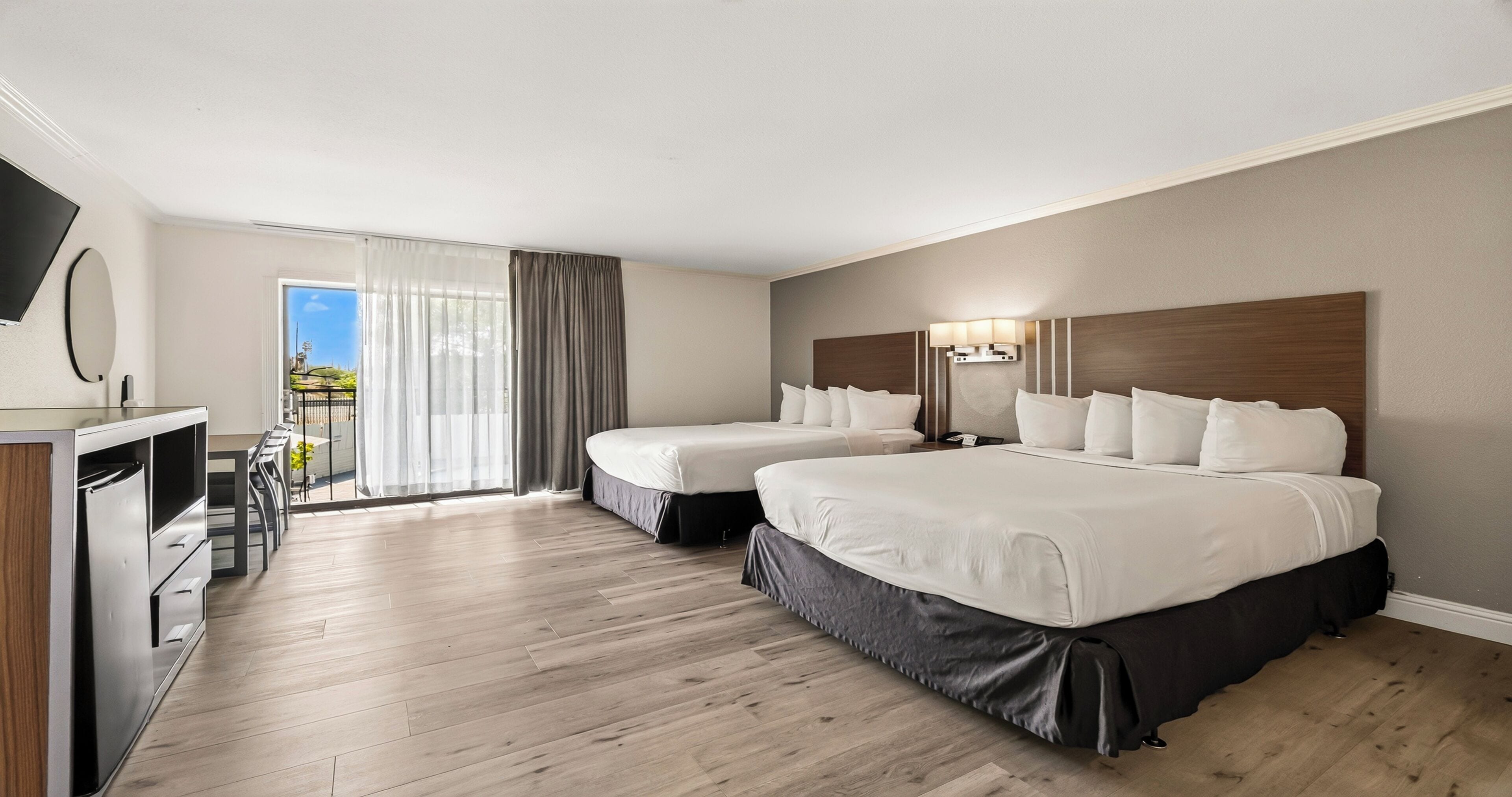 Habitación de hotel con dos camas, un escritorio y un balcón con cortinas.
