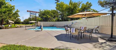 An outdoor pool area with lounge chairs and umbrellas, a Heritage Inn sign, and a wooden fence.
