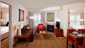 Une chambre d’hôtel avec un canapé, un fauteuil rouge, une table à manger et une cheminée.