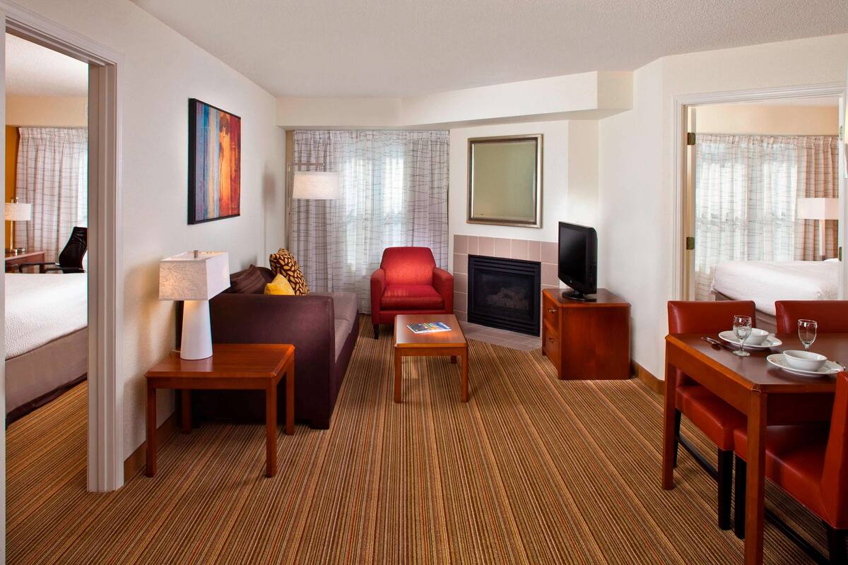 Une chambre d’hôtel avec un canapé, un fauteuil rouge, une table à manger et une cheminée.