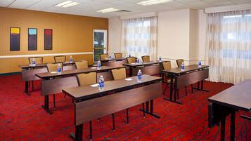 A conference room with multiple tables and chairs, equipped with water bottles, arranged on a red carpeted floor.
