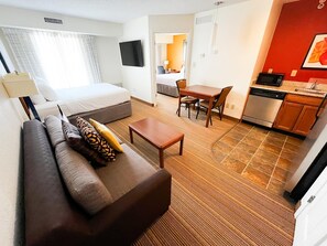 Een hotelkamer met een bed, bank, eettafel, keukenhoek en een aan de muur bevestigde televisie.