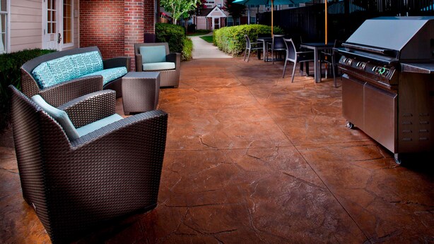 Une terrasse extérieure aménagée avec des meubles en osier, un barbecue et des parasols.
