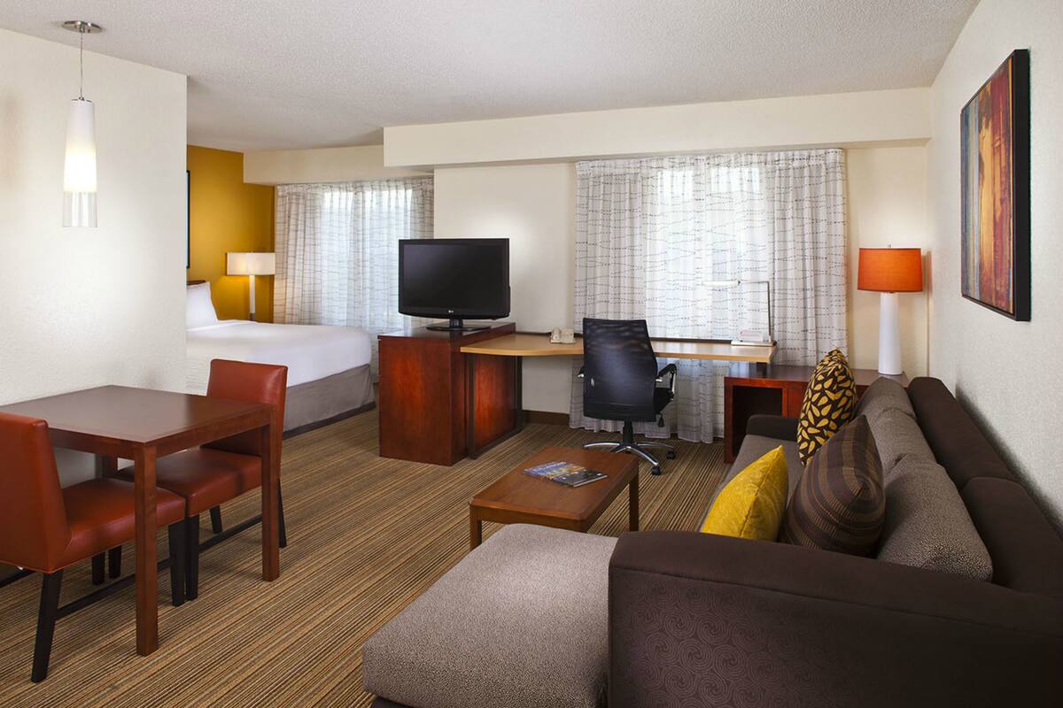 Une chambre d’hôtel comprenant un lit, un bureau avec un ordinateur, une télévision, un canapé et une table à manger avec des chaises.