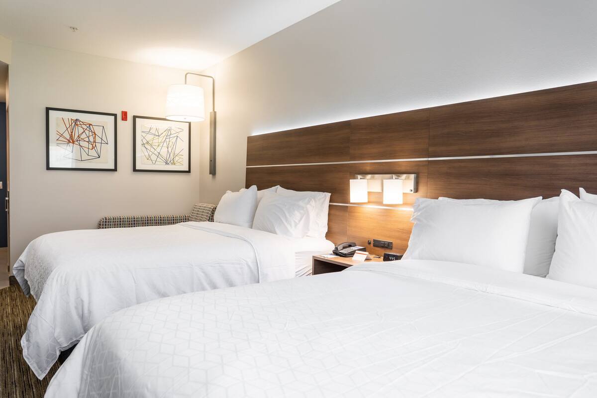 A hotel room with two beds, a wooden headboard, a nightstand with a phone, and two wall-mounted lamps.