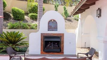 An outdoor patio with a fireplace, two wicker chairs, and a small table.