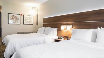 A hotel room with two beds, a wooden headboard, a nightstand with a phone, and two wall-mounted lamps.