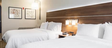 A hotel room with two beds, a wooden headboard, a nightstand with a phone, and two wall-mounted lamps.