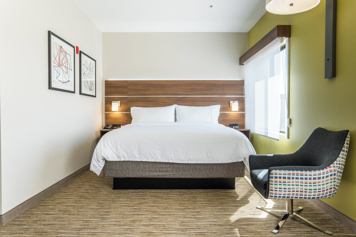 A hotel room with a bed, a chair, and two wall-mounted lamps.