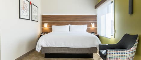 Una habitación de hotel moderna con una cama grande, una silla y dos lámparas de pared.