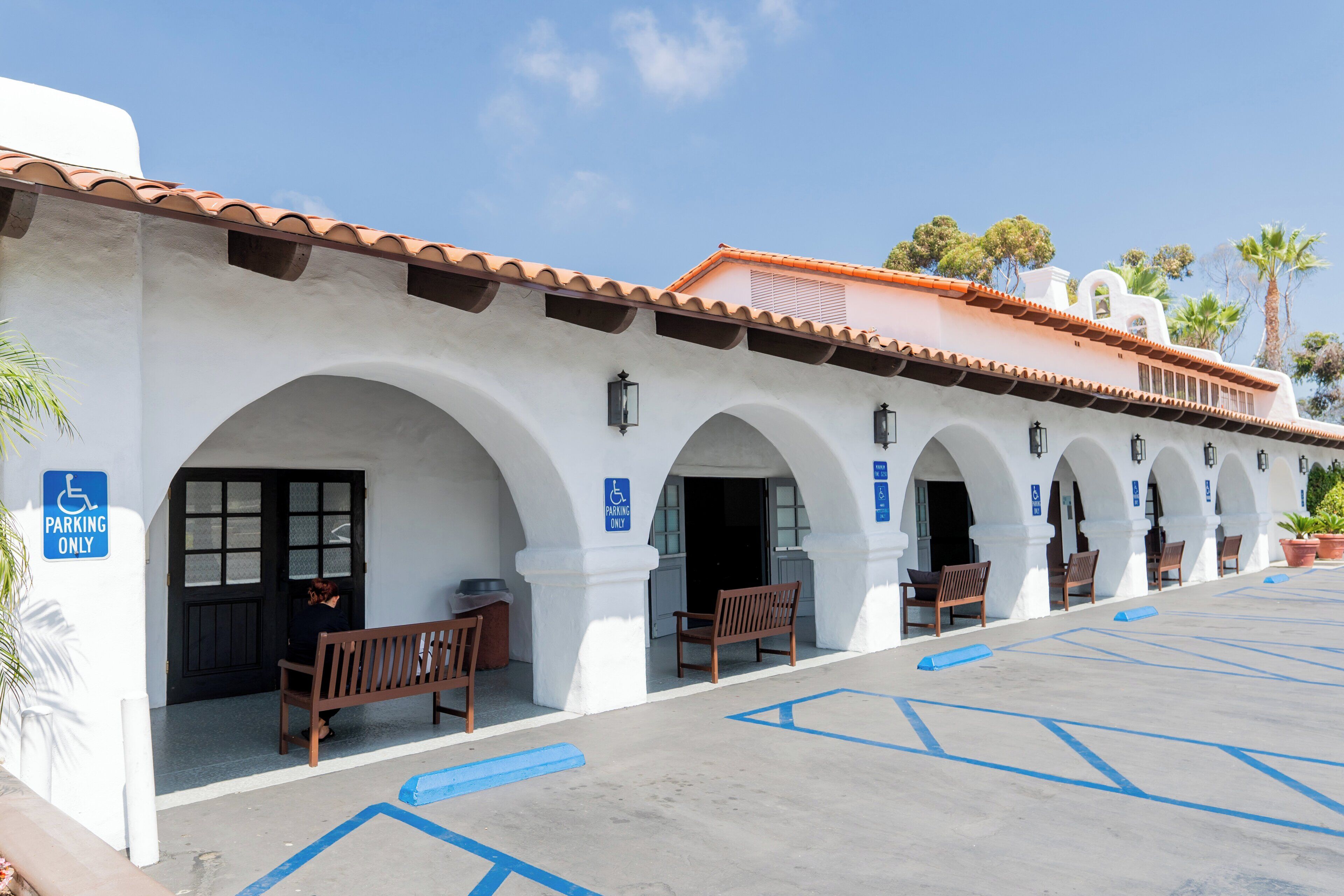 A building with white walls and terracotta roof tiles, featuring multiple arches and benches.
