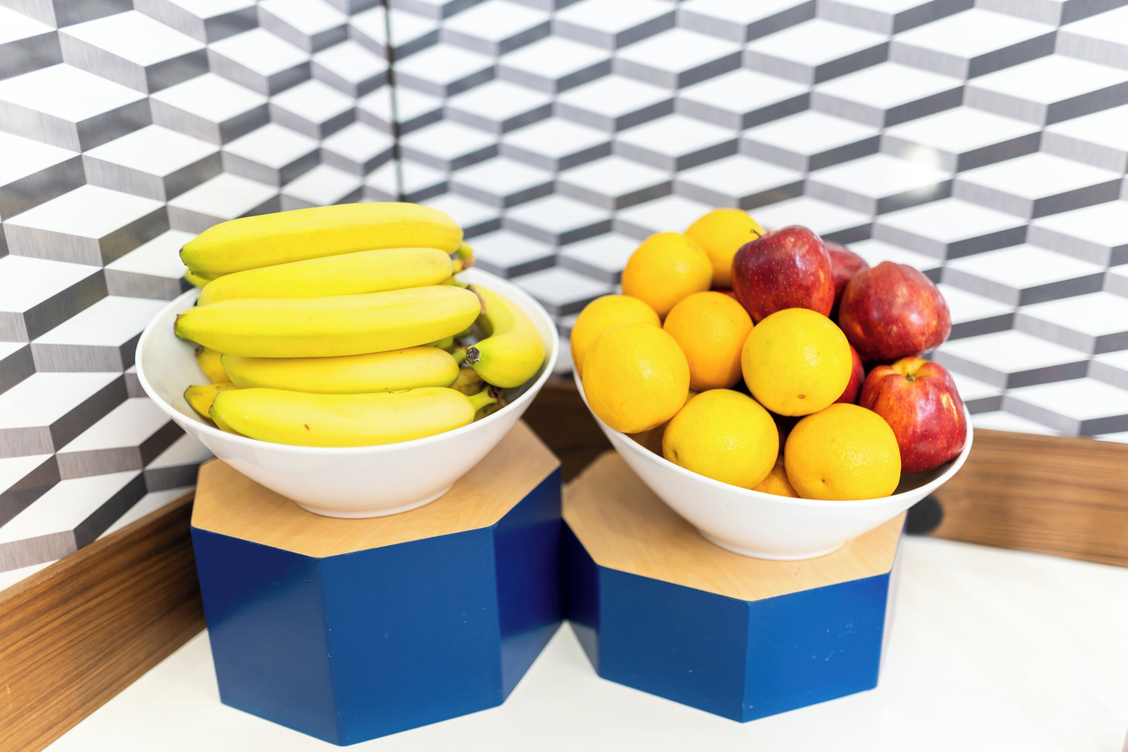 Two bowls of fruit on a table with a geometric patterned floor.