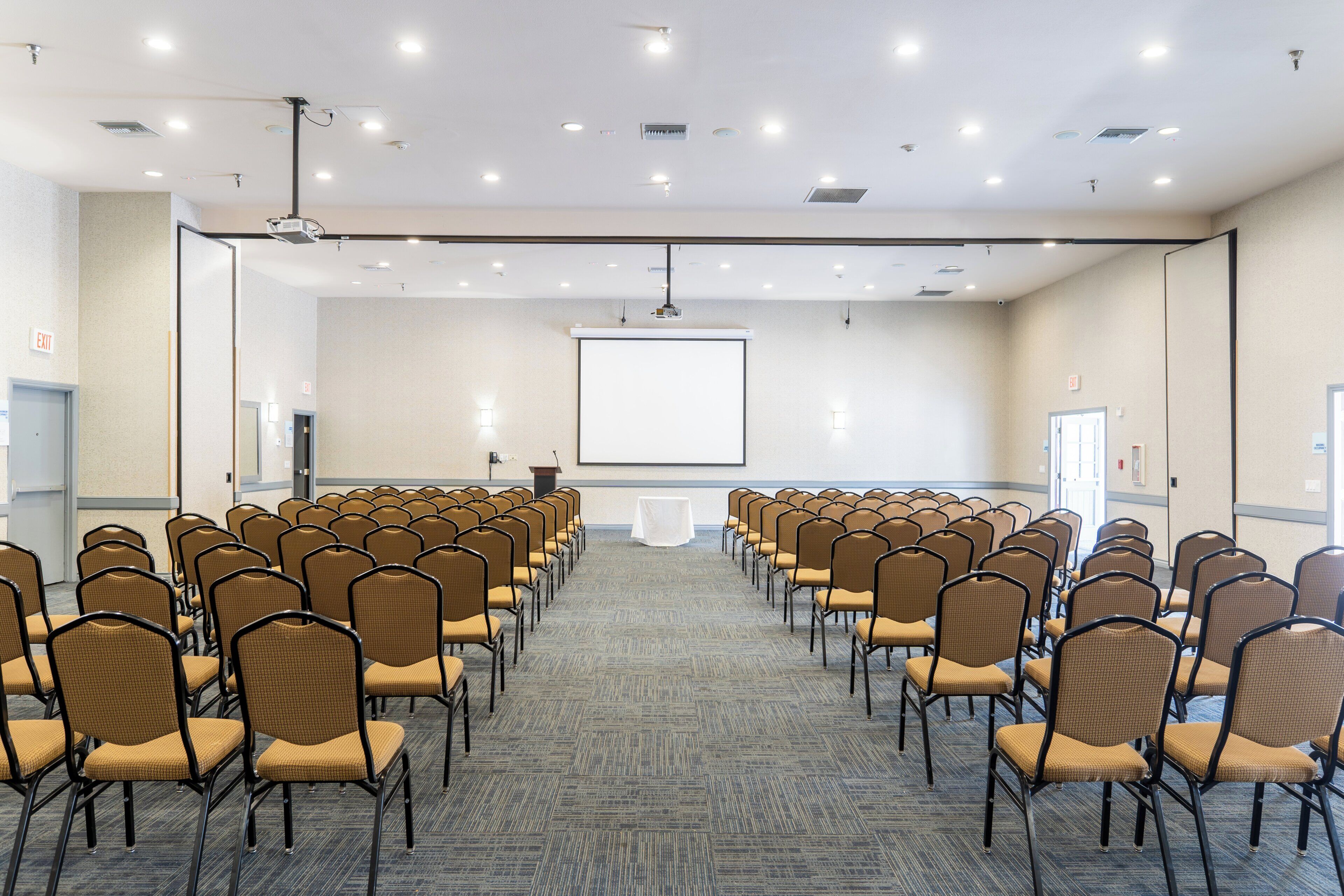 Ein Konferenzraum mit Reihen von Stühlen, einem Rednerpult und einer großen Leinwand im vorderen Bereich.