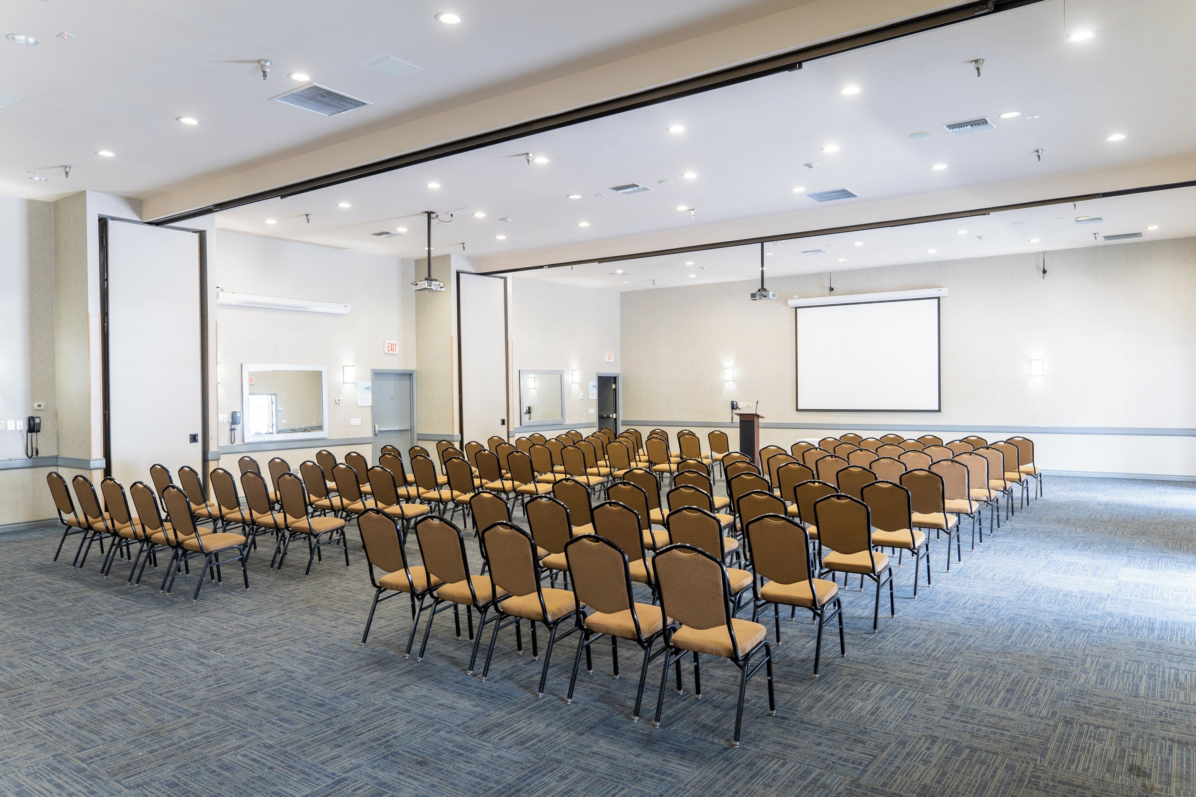 Une salle de conférence avec des rangées de chaises, un écran de projection et un pupitre.