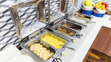 Un buffet proposant une variété de plats, notamment des œufs brouillés, des saucisses et d’autres mets.