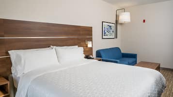Una habitación de hotel con una cama grande, un sillón azul, una mesita de noche y una lámpara de pared.