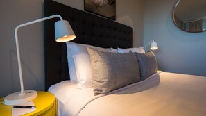 A neatly made bed with a tufted headboard, two bedside lamps, and a yellow nightstand with a pen and paper.