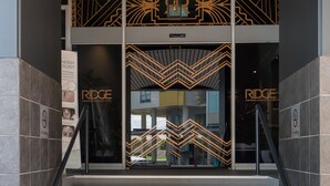 A staircase leading to a building entrance with geometric patterns and the word "RIDGE" on the glass doors. - The Ridge Apartment Hotel (Spring Hill)