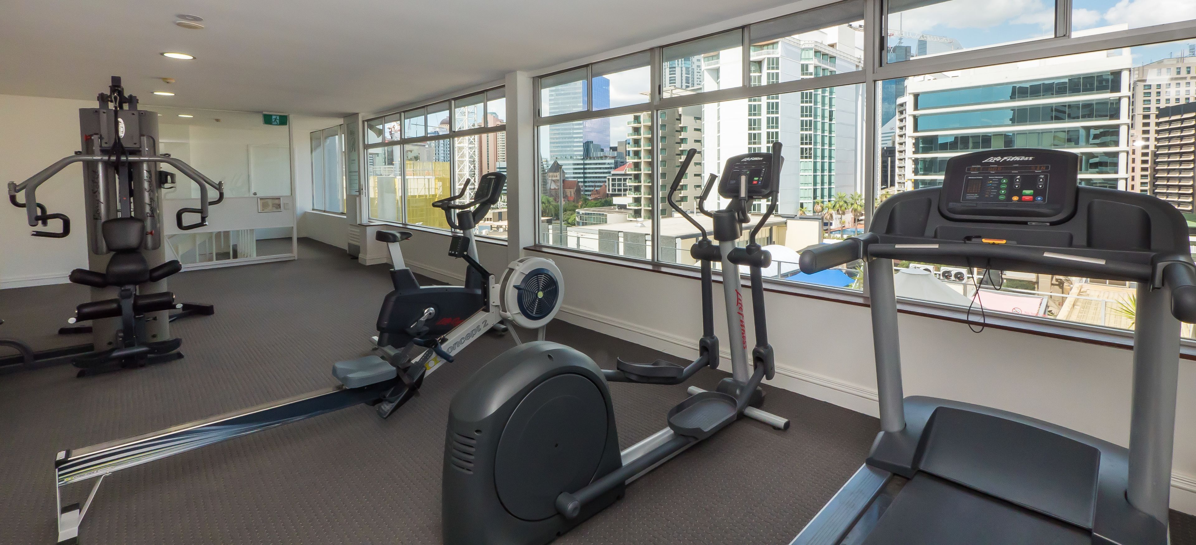 Uma academia com máquinas de cardio, equipamentos de peso e amplas janelas com vista para a cidade.