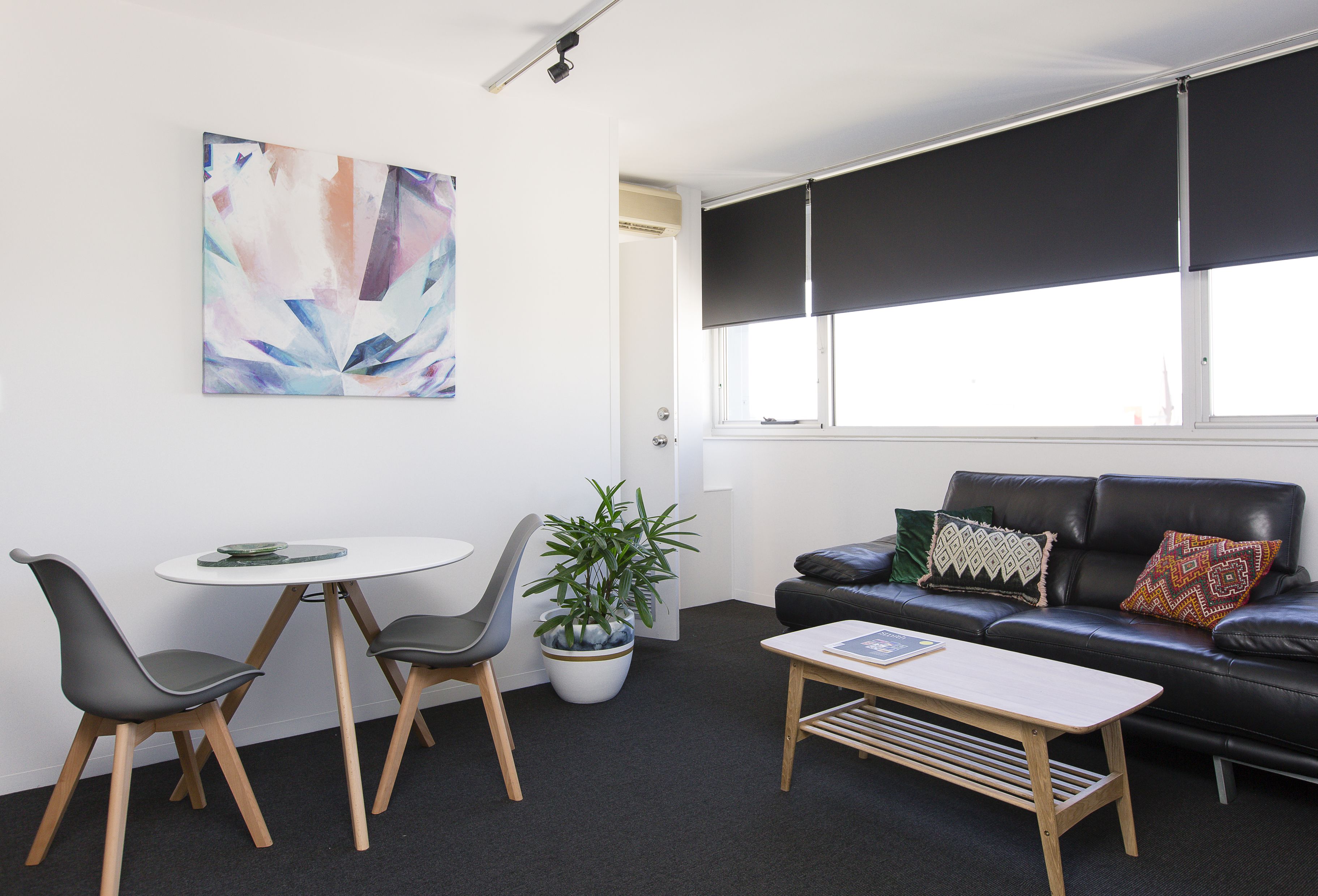 Una sala de estar moderna con un sofá de cuero negro, dos sillones grises, una mesa de centro blanca y una planta en maceta.