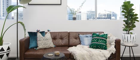 A modern living room with a brown leather sofa, a round black coffee table, and a city view through large windows.