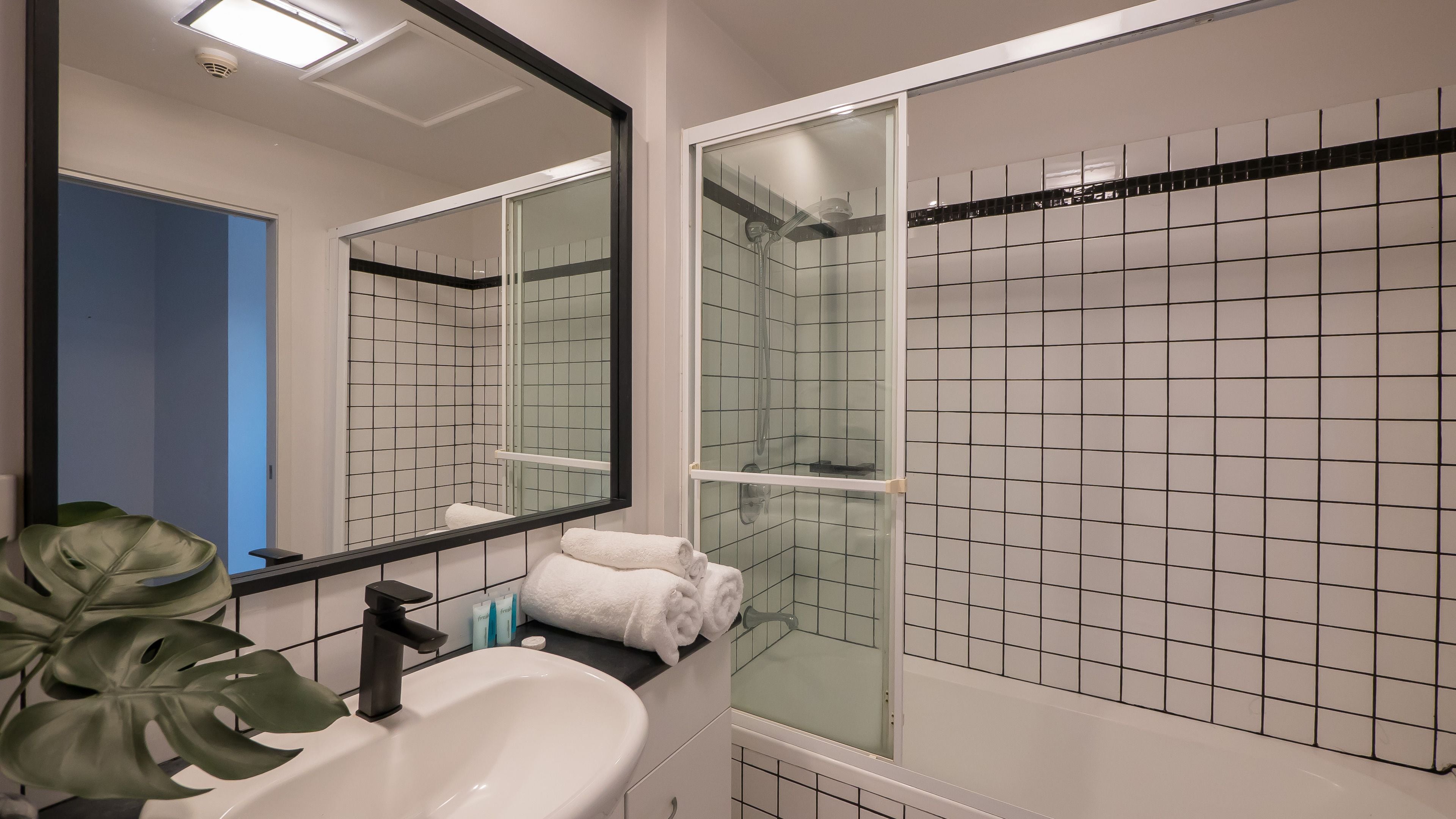 A bathroom with a white sink, a mirror, a shower with a glass door, and a potted plant.