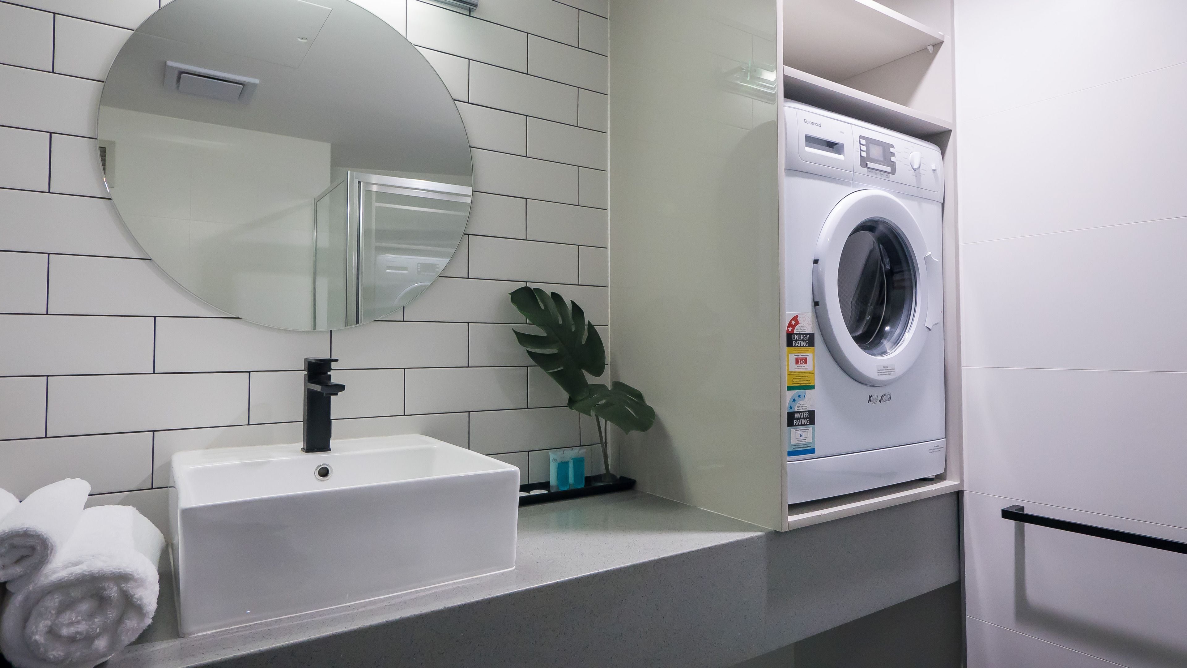 A modern bathroom with a white sink, mirror, and a front-loading washing machine.