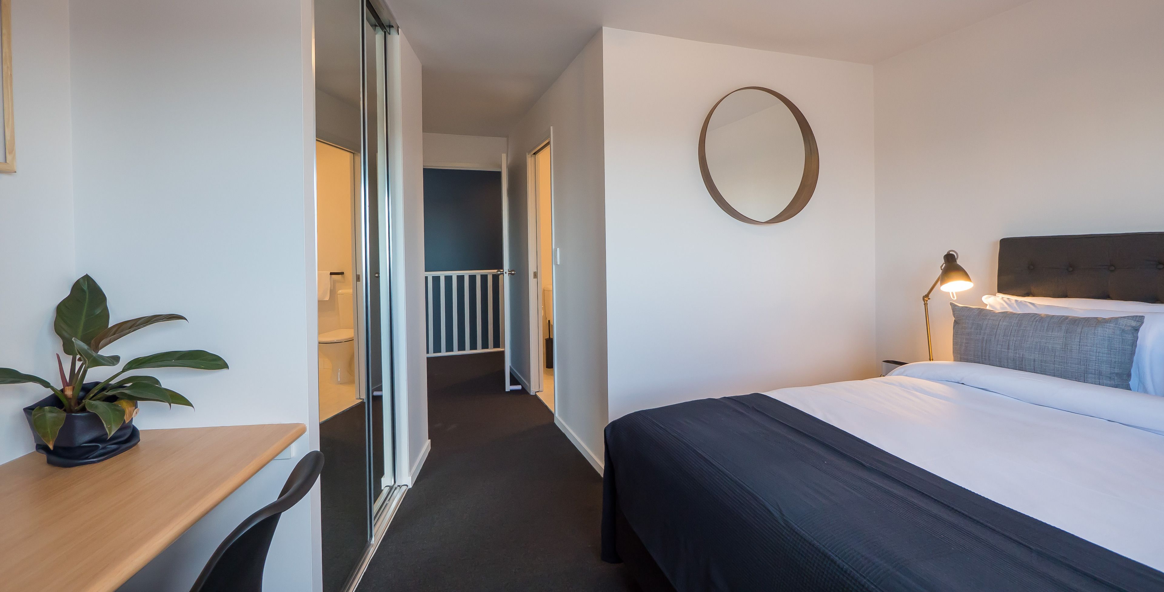 A hotel room with a bed, bedside lamp, and a potted plant.