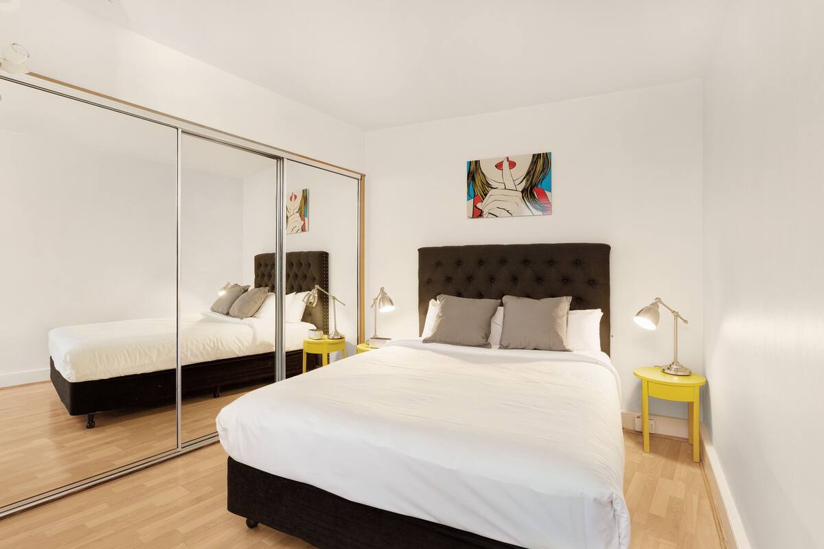 Une chambre à coucher avec un grand lit, un miroir, une table de chevet et un tableau accroché au mur.